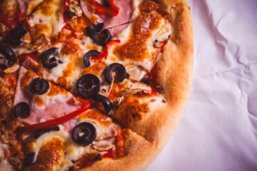 Pizza cu sunca, ciuperci și măsline negre.